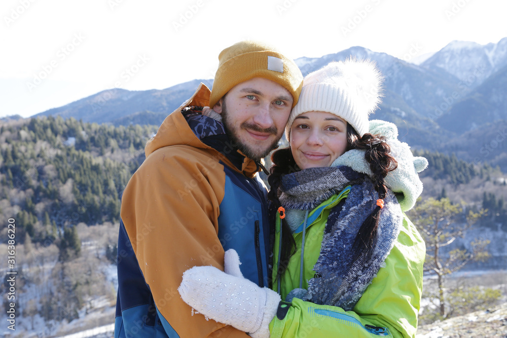 Young couple man and woman in bright clothes hugging on the background of snow and a winter landscape in the mountains. Winter concept. The concept of love and relationships.