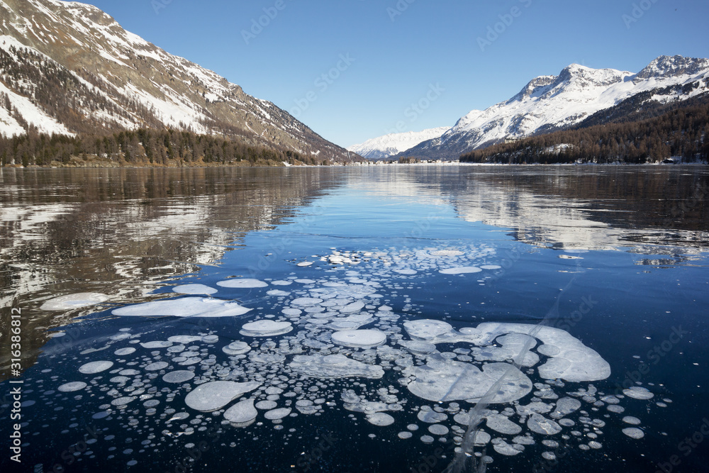 Trapped methane bubbles under the frozen lake with landscape as background (focus stacking)
