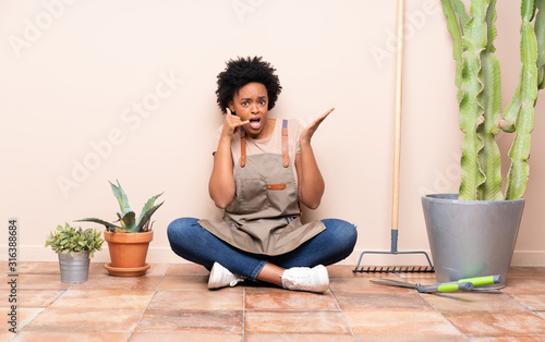 Gardener woman sitting on the floor making phone gesture and doubting