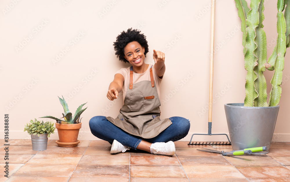 Gardener woman sitting on the floor points finger at you while smiling Gardener woman sitting on the floor points finger at you while smiling