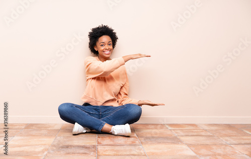 African american woman sitting on the floor holding copyspace to insert an ad
