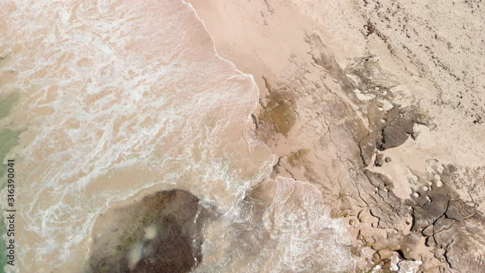 Ascending aerial over sand and rock beach with wave swash. Ascending aerial over sand and rock beach with wave swash.