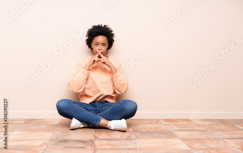 African american woman sitting on the floor showing a sign of silence gesture