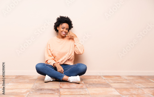 African american woman sitting on the floor making phone gesture. Call me back sign