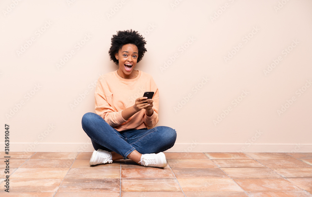 African american woman sitting on the floor surprised and sending a message African american woman sitting on the floor surprised and sending a message