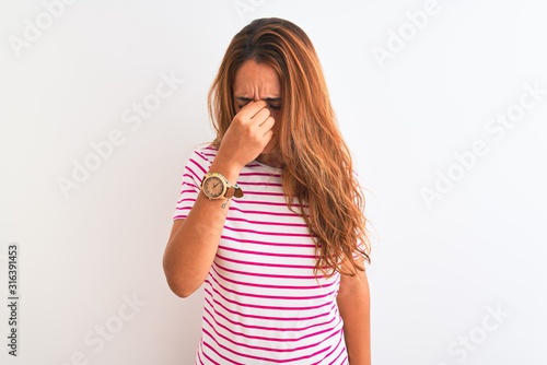 Young redhead woman wearing striped casual t-shirt stading over white isolated background tired rubbing nose and eyes feeling fatigue and headache. Stress and frustration concept.