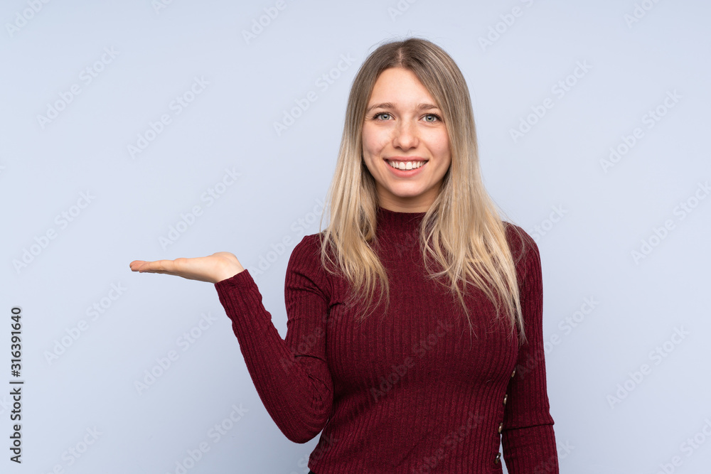 Young blonde woman over isolated blue background holding copyspace imaginary on the palm to insert an ad Young blonde woman over isolated blue background holding copyspace imaginary on the palm to insert an ad