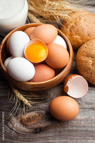 Raw broken egg with yolk in a wooden bowl. Fresh white and brown chicken eggs on wooden background