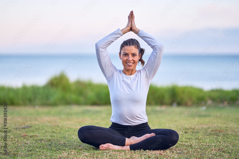 Young beautiful sportwoman smiling happy practicing yoga. Coach sitting with smile on face teaching prayer pose at park