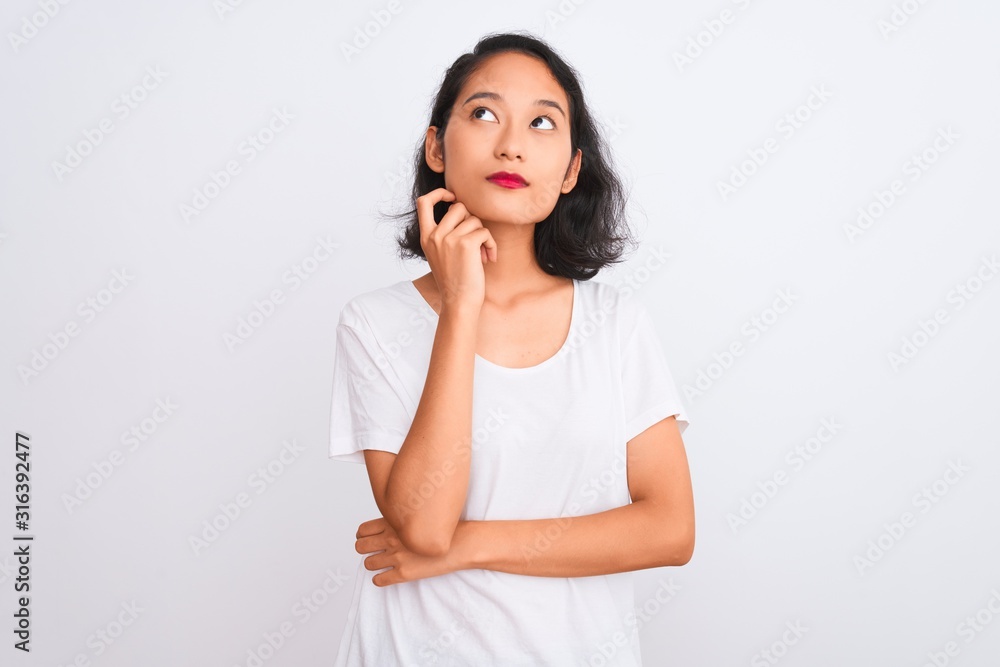 Young chinese woman wearing casual t-shirt standing over isolated white background with hand on chin thinking about question, pensive expression. Smiling with thoughtful face. Doubt concept. Young chinese woman wearing casual t-shirt standing over isolated white background with hand on chin thinking about question, pensive expression. Smiling with thoughtful face. Doubt concept.