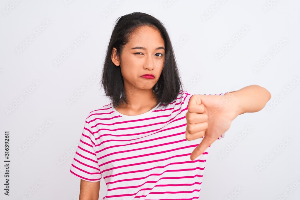Young chinese woman wearing striped t-shirt standing over isolated white background looking unhappy and angry showing rejection and negative with thumbs down gesture. Bad expression. Young chinese woman wearing striped t-shirt standing over isolated white background looking unhappy and angry showing rejection and negative with thumbs down gesture. Bad expression.