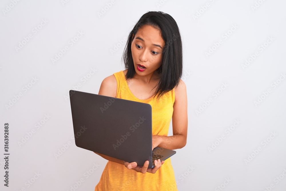 Young beautiful chinese woman using laptop standing over isolated white background scared in shock with a surprise face, afraid and excited with fear expression Young beautiful chinese woman using laptop standing over isolated white background scared in shock with a surprise face, afraid and excited with fear expression