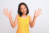 Young chinese woman wearing yellow casual t-shirt standing over isolated white background showing and pointing up with fingers number ten while smiling confident and happy.