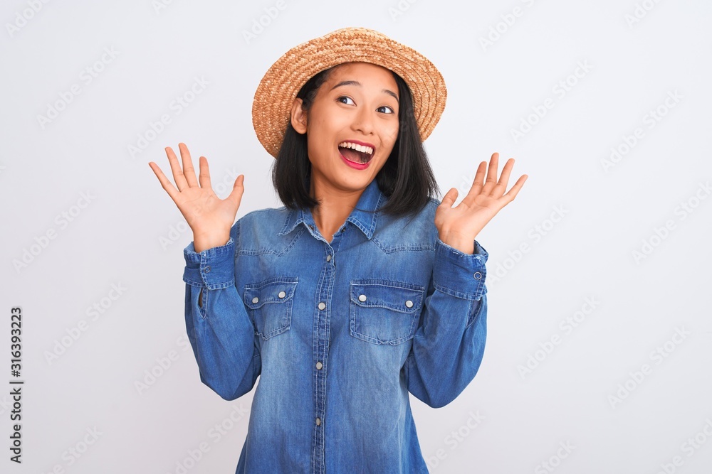 Young beautiful chinese woman wearing denim shirt and hat over isolated white background celebrating crazy and amazed for success with arms raised and open eyes screaming excited. Winner concept Young beautiful chinese woman wearing denim shirt and hat over isolated white background celebrating crazy and amazed for success with arms raised and open eyes screaming excited. Winner concept