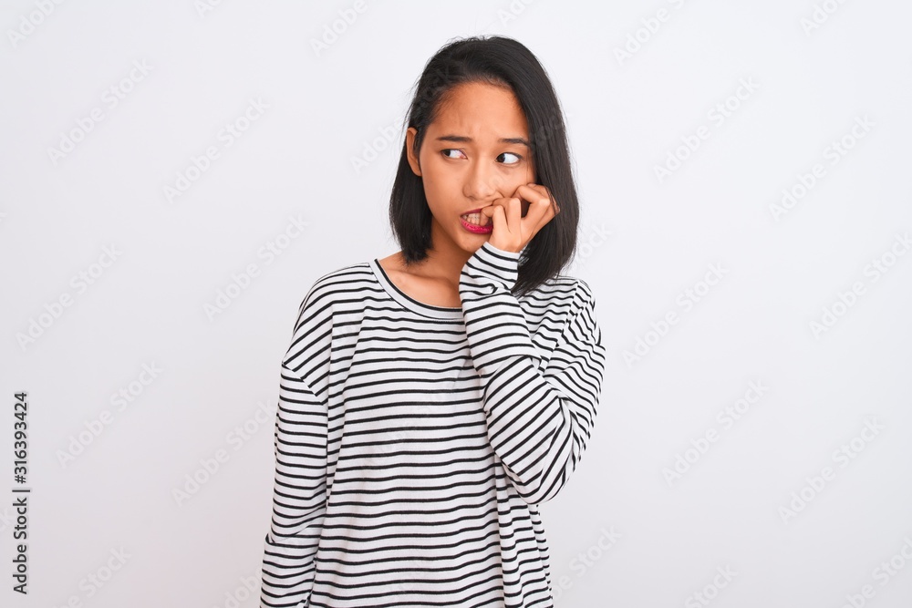 Young chinese woman wearing striped t-shirt standing over isolated white background looking stressed and nervous with hands on mouth biting nails. Anxiety problem. Young chinese woman wearing striped t-shirt standing over isolated white background looking stressed and nervous with hands on mouth biting nails. Anxiety problem.
