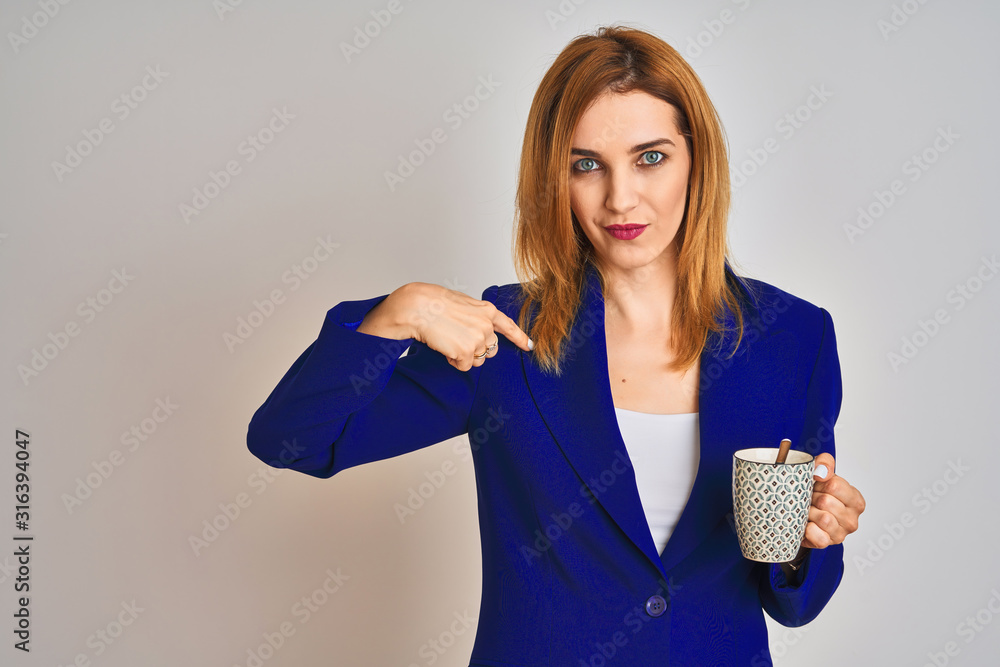 Redhead caucasian business woman drinking a cup of coffee over isolated background with surprise face pointing finger to himself Redhead caucasian business woman drinking a cup of coffee over isolated background with surprise face pointing finger to himself