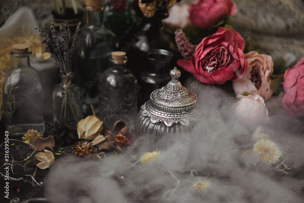 vintage jars, bottles, containers, flowers in smoke and dry leaves on a wooden table with warm light