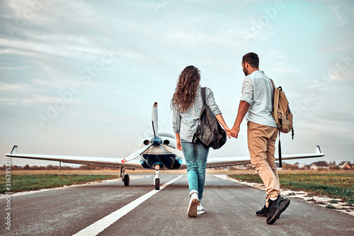 Back view of beautiful romantic couple holding hands while walking on take-off ground near the aircraft