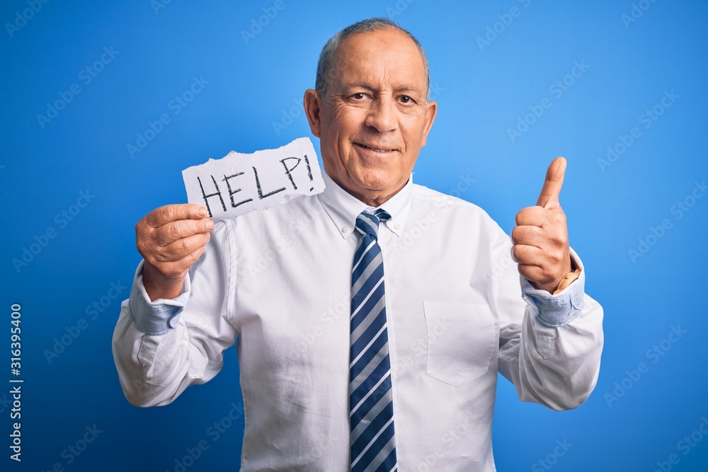 Senior handsome businessman holding paper help message over isolated blue background happy with big smile doing ok sign, thumb up with fingers, excellent sign Senior handsome businessman holding paper help message over isolated blue background happy with big smile doing ok sign, thumb up with fingers, excellent sign