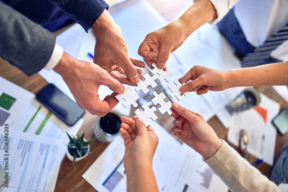 Group of business workers with hands together connecting pieces of puzzle at the office