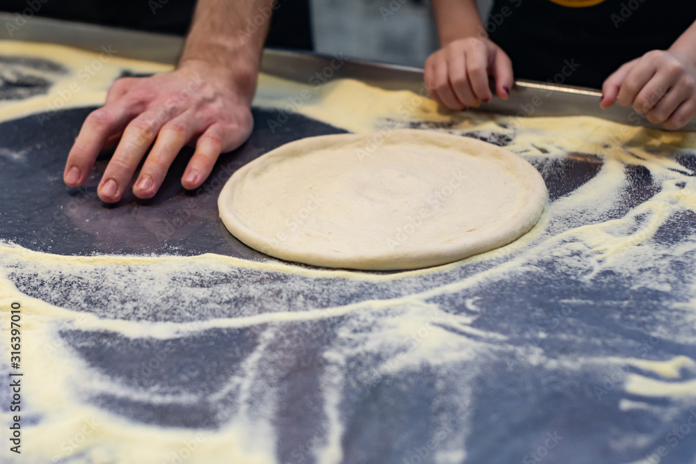 The chef in black apron makes pizza dough with your hands on the table. The chef in black apron makes pizza dough with your hands on the table.