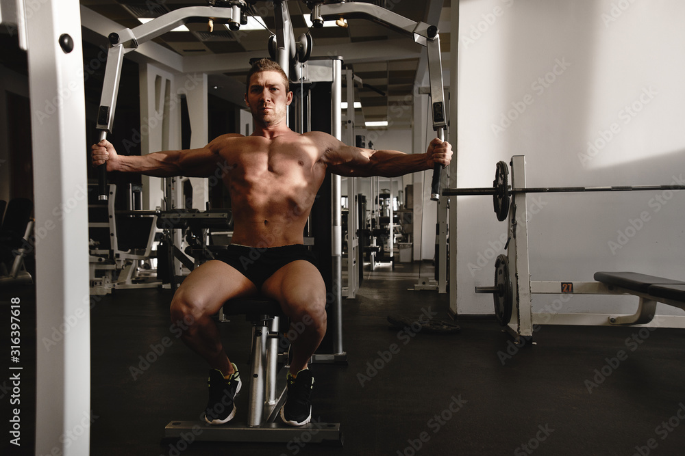 Fototapeta premium Portrait of fitness athlete man with muscular body does exercises on sports equipment in the gym, workout arm muscles, pumping biceps and triceps