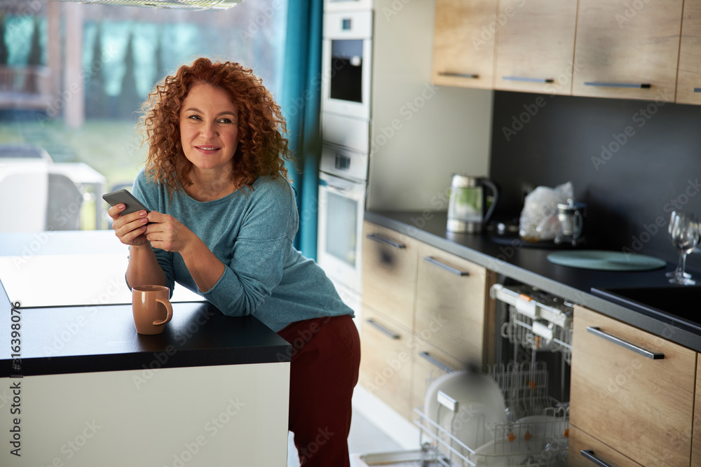 Relaxed woman with cellphone in kitchen stock photo Relaxed woman with cellphone in kitchen stock photo