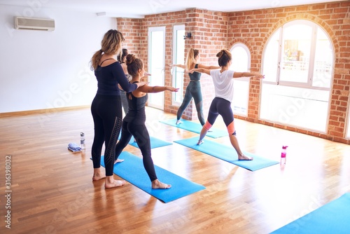 Young beautiful group of sportswomen practicing yoga. Coach teaching stretch to sporty women at gym