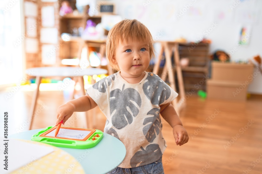 Adorable toddler drawing using digital board around lots of toys at kindergarten Adorable toddler drawing using digital board around lots of toys at kindergarten