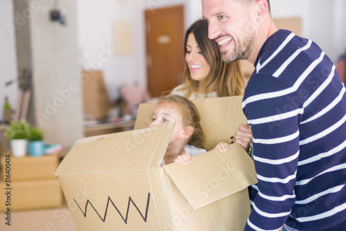 Beautiful famiily, kid playing with his parents riding fanny cardboard box at new home photo