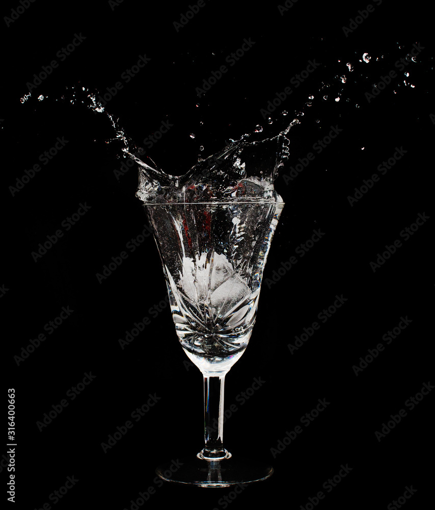Glass cup with water splashes and ice cubes in the dark room Glass cup with water splashes and ice cubes in the dark room