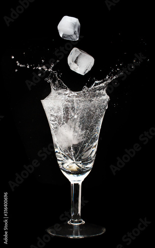 Glass cup with water splashes and ice cubes in the dark room