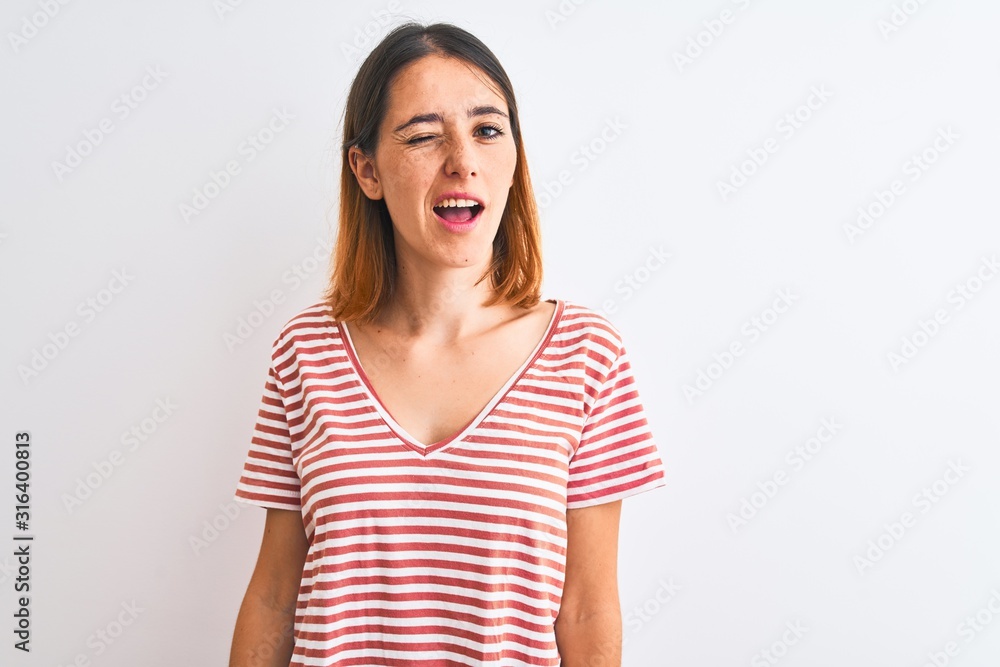 Beautiful redhead woman wearing casual striped red t-shirt over isolated background winking looking at the camera with sexy expression, cheerful and happy face. Beautiful redhead woman wearing casual striped red t-shirt over isolated background winking looking at the camera with sexy expression, cheerful and happy face.