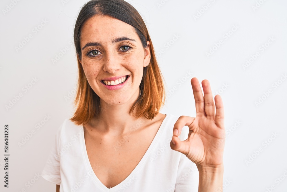 Beautiful redhead woman wearing casual white t-shirt over isolated background doing ok sign with fingers, excellent symbol Beautiful redhead woman wearing casual white t-shirt over isolated background doing ok sign with fingers, excellent symbol
