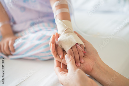 Little girl was sick and her hand was hold by her mother in hospital room. Selective focus,