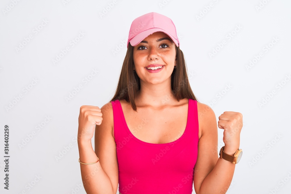 Young beautiful girl wearing pink casual t-shirt and cap over isolated white background celebrating surprised and amazed for success with arms raised and open eyes. Winner concept. Young beautiful girl wearing pink casual t-shirt and cap over isolated white background celebrating surprised and amazed for success with arms raised and open eyes. Winner concept.