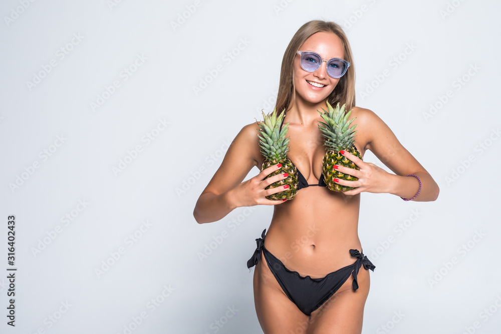 Obraz premium Young woman in swimsuit holding a pineapple with sunglasses isolated gray background