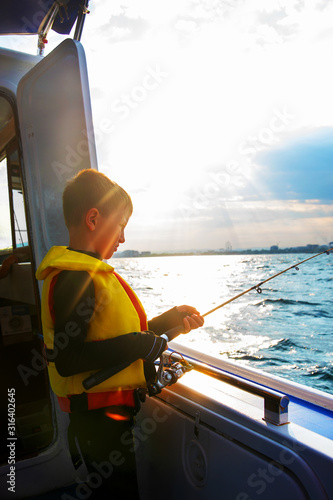 Little boy fishing on a fishing rod from a boat at sunset