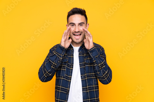 Young handsome man over isolated yellow background shouting with mouth wide open © luismolinero