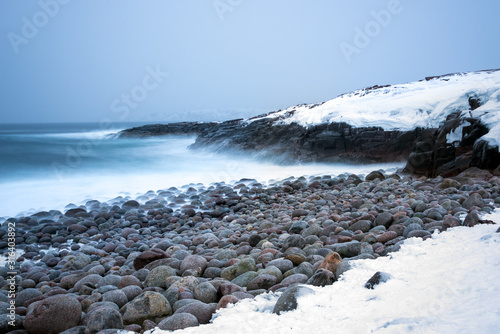 Long exposure of surf breaking on snow covered rocky shores and large stone boulders in the Polar region above the Arctic Circle