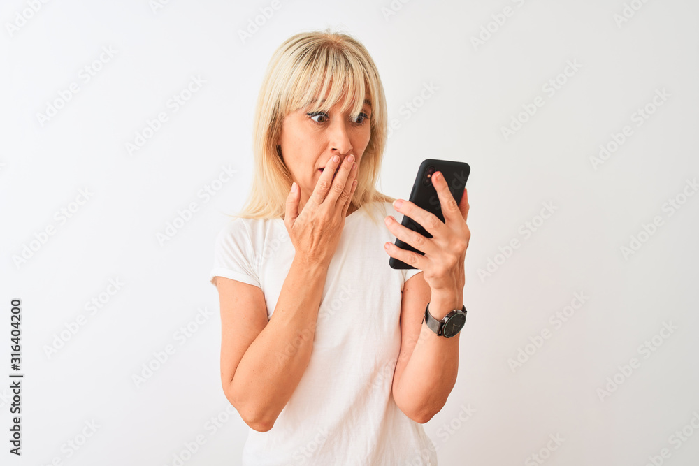 Middle age woman using smartphone standing over isolated white background cover mouth with hand shocked with shame for mistake, expression of fear, scared in silence, secret concept Middle age woman using smartphone standing over isolated white background cover mouth with hand shocked with shame for mistake, expression of fear, scared in silence, secret concept