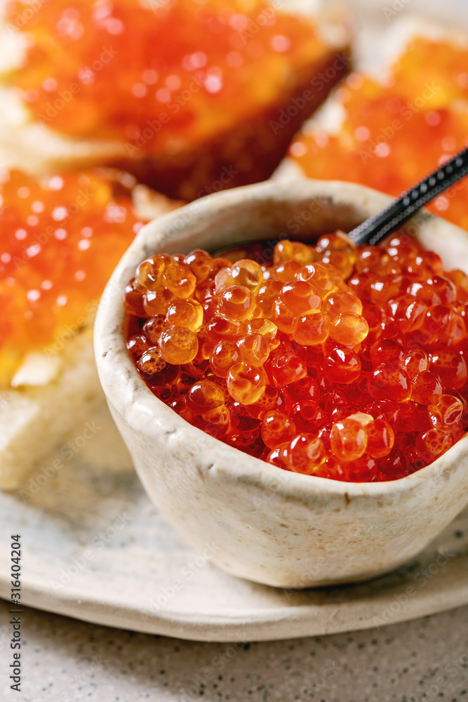 Red salmon caviar in bowl and on wheat bread, served on ceramic plate over grey spotted kitchen table. Close up Red salmon caviar in bowl and on wheat bread, served on ceramic plate over grey spotted kitchen table. Close up