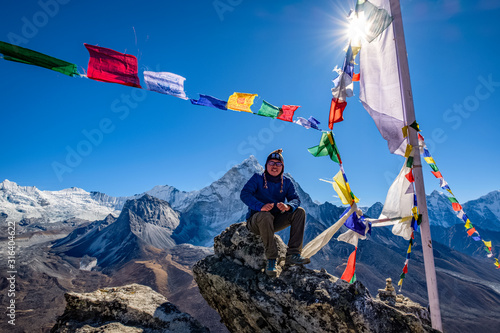 Asian hiker sitting on the cliff in Nangkartsang Peak, Everest Base Camp, with clear blue sky and himalayan mountain range at the background. photo