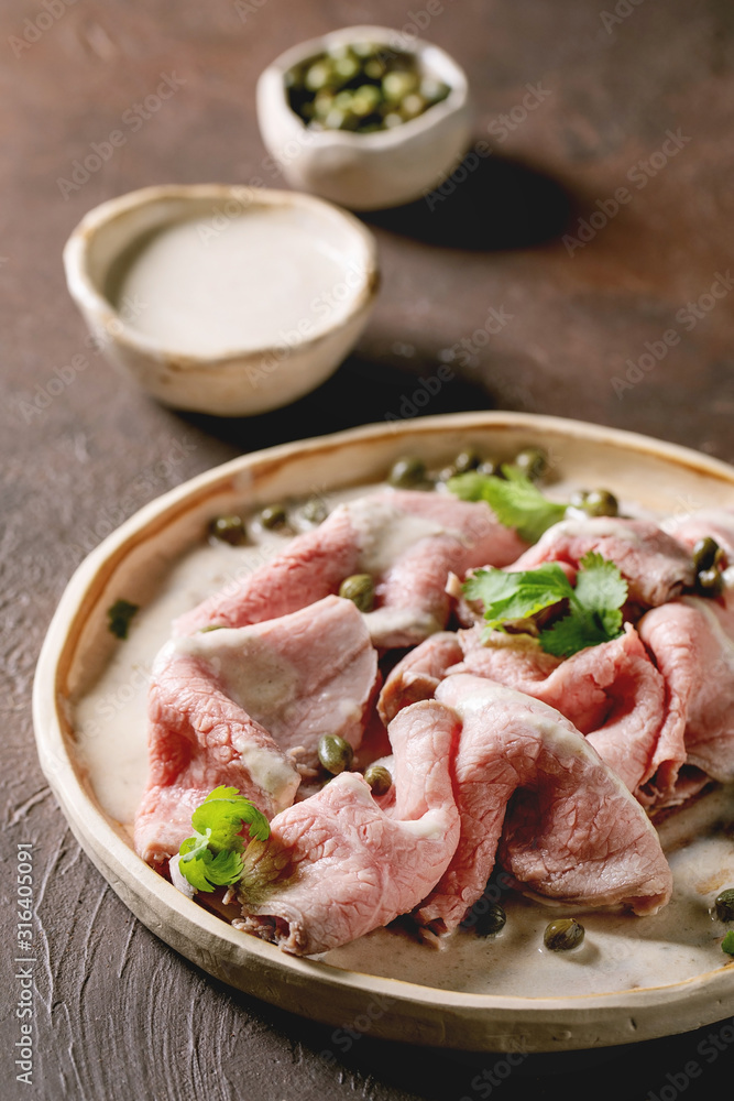 Vitello tonnato italian dish. Thin sliced veal with tuna sauce, capers and coriander served on ceramic plate over dark texture background.