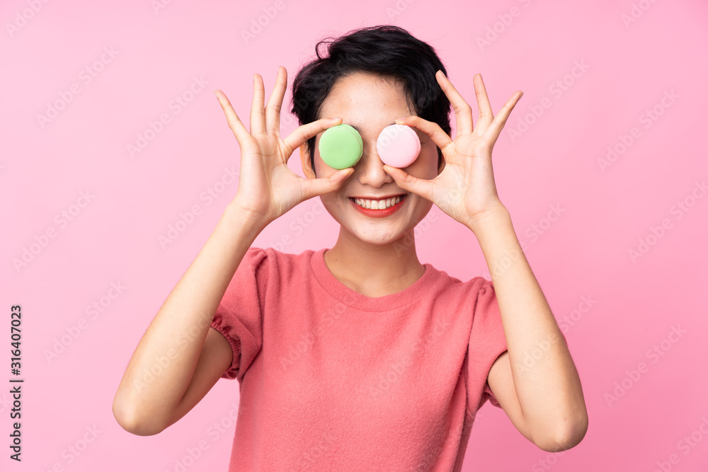 Young Asian girl over isolated pink background wearing colorful French macarons as glasses