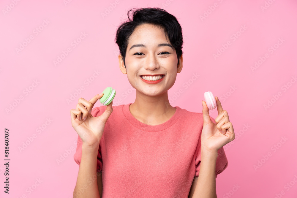 Young Asian girl over isolated pink background holding colorful French macarons Young Asian girl over isolated pink background holding colorful French macarons