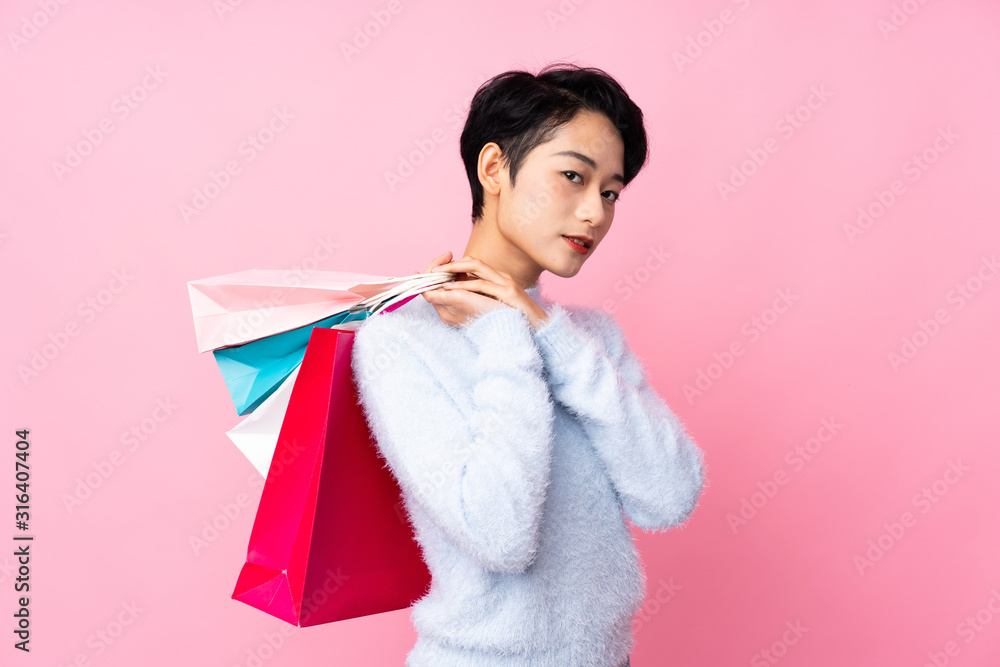 Young Asian girl over isolated pink background holding shopping bags Young Asian girl over isolated pink background holding shopping bags