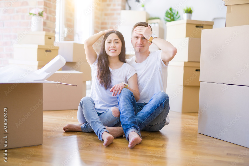 Young beautiful couple sitting on the floor at new home around cardboard boxes stressed with hand on head, shocked with shame and surprise face, angry and frustrated. Fear and upset for mistake. Young beautiful couple sitting on the floor at new home around cardboard boxes stressed with hand on head, shocked with shame and surprise face, angry and frustrated. Fear and upset for mistake.