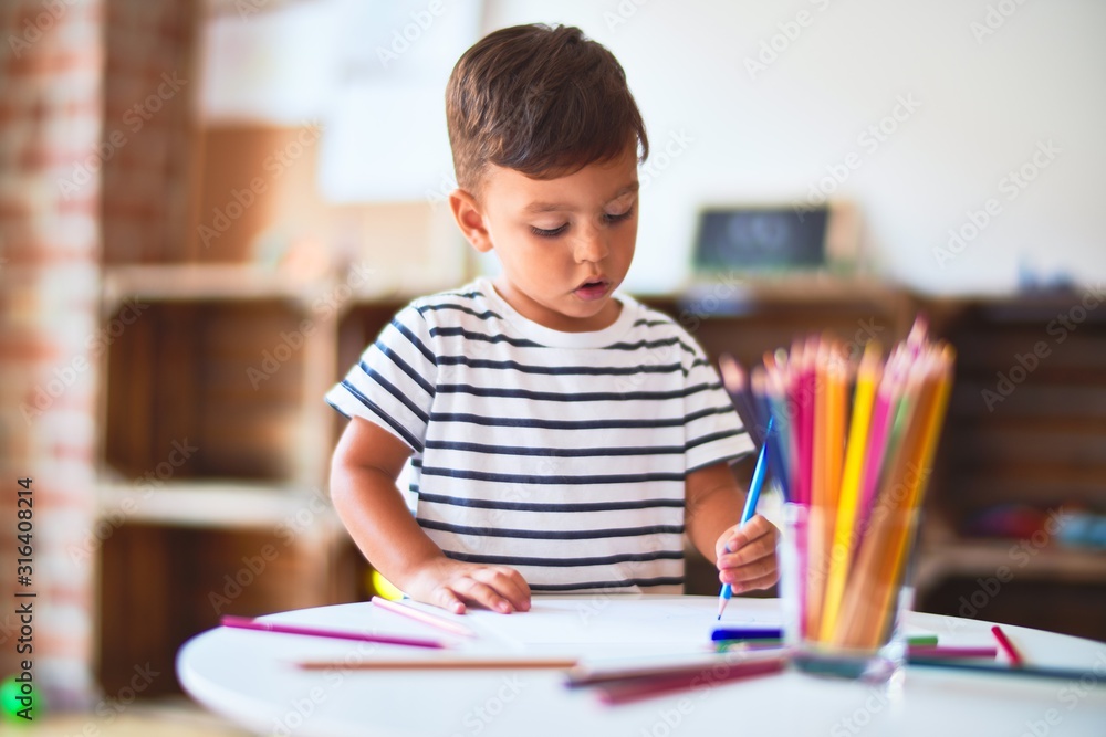 Beautiful toddler boy drawing cute draw using colored pencils at kindergarten Beautiful toddler boy drawing cute draw using colored pencils at kindergarten