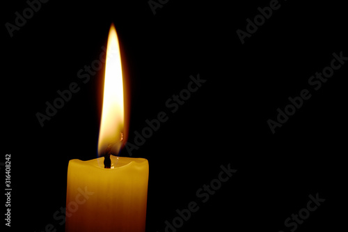 Eine brennende weiße Kerze mit großer, gelber Flamme isoliert auf schwarzem Hintergrund mit Platz für Text